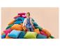 Fille souriante assise sur une pile de coussins colorés.