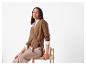Vrouw in een bruin wikkelvest en beige broek, zittend op een stoel.