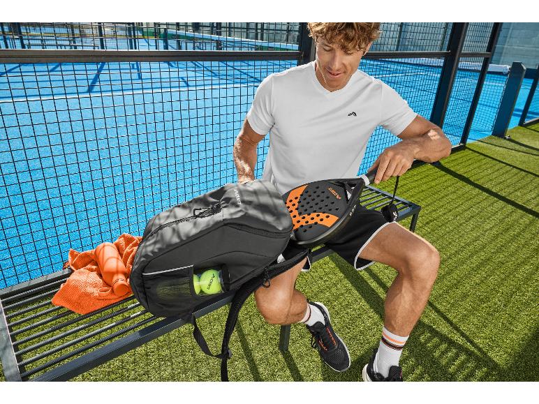 Man op padelbaan met rugzak, padelracket, bal en waterfles.