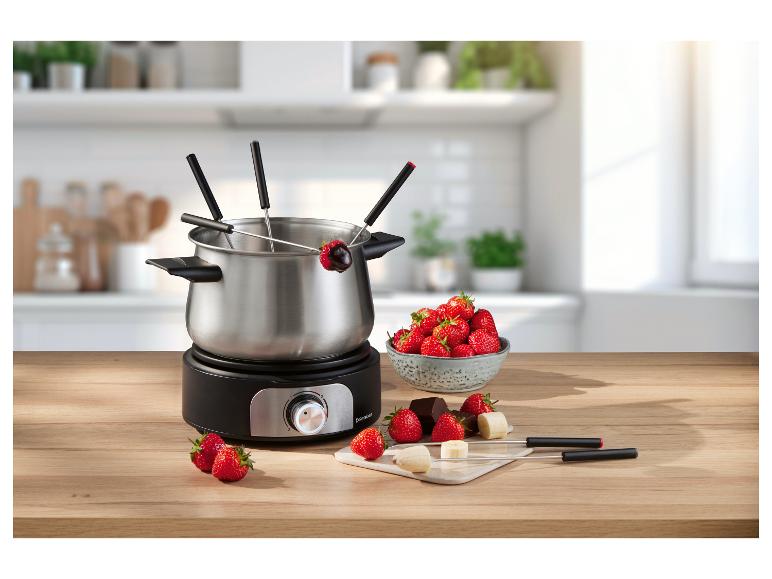 Elektrische fondueset met aardbeien, chocolade en bananen op een houten tafel.