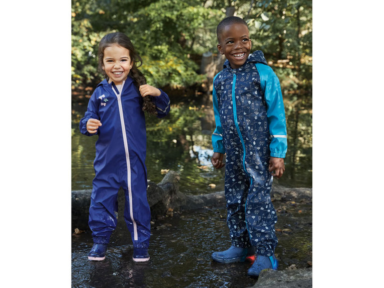 Deux enfants portant des combinaisons de pluie à motifs de bateaux, jouent dans une flaque d'eau.