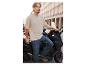 Un homme porte un t-shirt beige clair et un jean bleu, tout en s'appuyant sur un scooter.