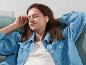 Femme se relaxant sur un canapé, écoutant de la musique avec des écouteurs intra-auriculaires blancs.