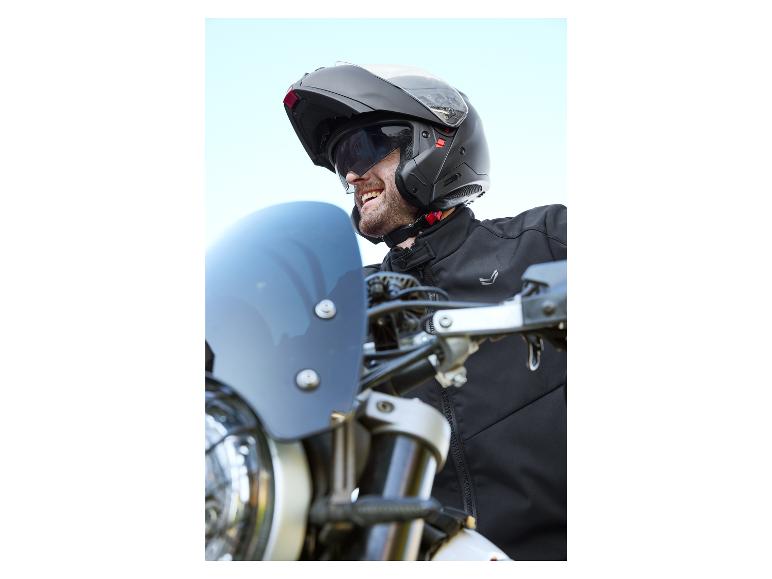 Un motard porte un casque noir et une veste sur une moto.