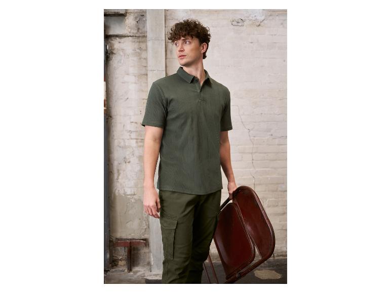 Man in een groene poloshirt en cargobroek, met een opvouwbare stoel.