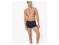 Man poseert tegen een witte achtergrond, draagt marineblauwe boxershorts met witte patronen.