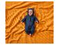 Baby in donkerblauw berenpak op een oranje wafeldekentje.