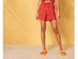 Vrouw draagt oranje slippers en korte broek met een abstract patroon.