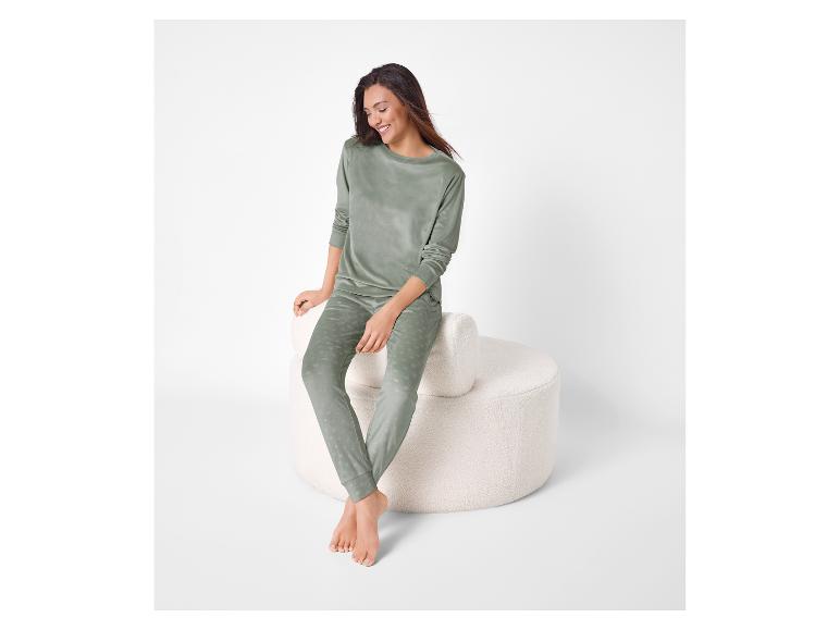 Vrouw in groene velours pyjama met stippen, zittend op een witte poef.