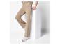 Vrouw in beige gebreide set met broek en trui, staand bij een witte doos.
