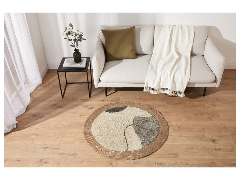 Een ronde jute vloerkleed met een abstract motief voor een witte bank met een wit deken.