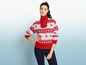 Een vrouw draagt ​​een rode trui met een ski-print en blauwe jeans.