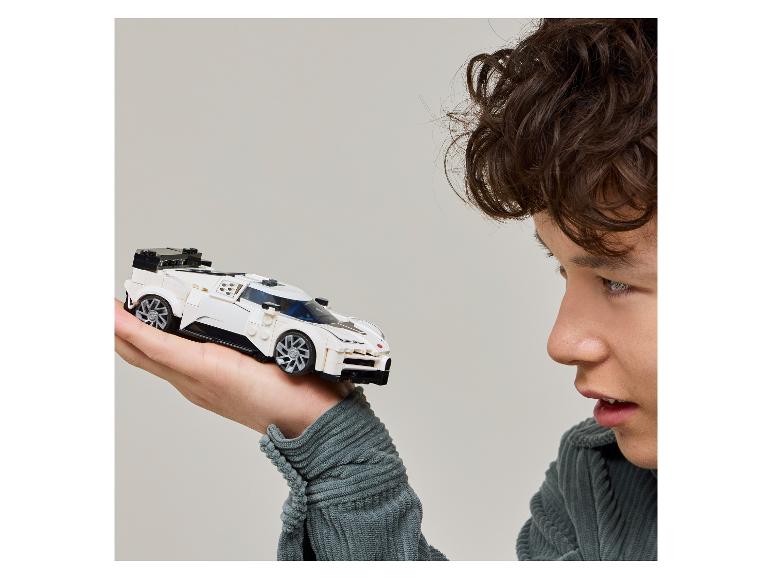 Een jonge man kijkt naar een witte miniatuur raceauto die hij in zijn hand houdt.