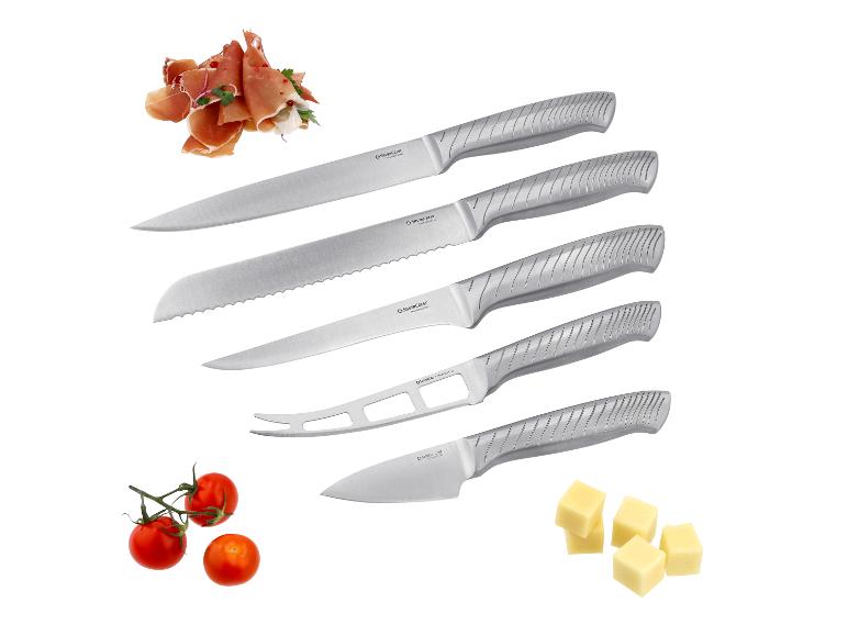 Set van vijf roestvrijstalen messen met getextureerde handgrepen, naast prosciutto, cherrytomaten en kaasblokjes.