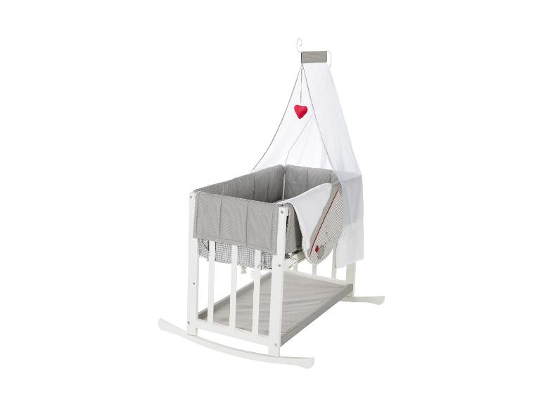 Witte schommelwieg met grijs beddengoed en hemel.