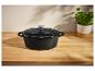 Zwarte gietijzeren pan met deksel op een houten tafel.