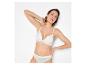 Vrouw in witte kanten bralette en slip, poserend tegen een witte achtergrond.
