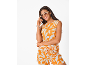 Femme souriante en haut et short orange à motif floral blanc, lunettes de soleil et créoles.