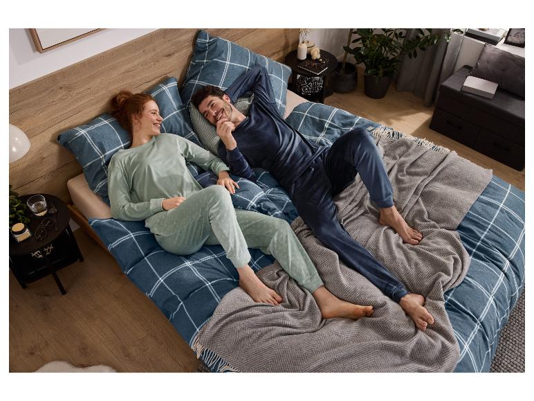 Een lachend stel ontspant in bed, gekleed in bijpassende pyjama's, met geruit beddengoed.