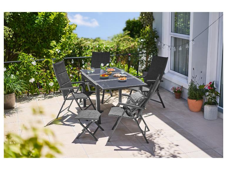 Mobilier de terrasse: table, chaises et tabourets en extérieur, entourés de plantes.