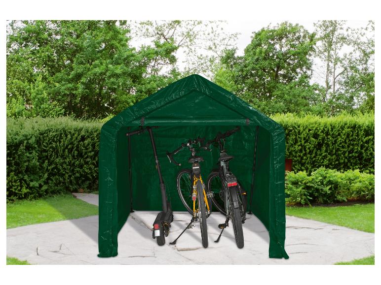Un abri vert pour vélos et trottinettes dans une cour avec pelouse et arbustes.