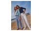 Twee vrouwen in casual jeans en tops op een zandstrand met een boot op de achtergrond.