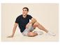 Homme en t-shirt noir et short gris assis par terre, souriant et regardant vers le haut.