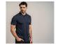 Man in een marineblauw poloshirt en zwarte broek, poserend met hand in zak.