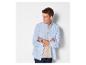 Man in blauw overhemd en beige T-shirt, met gekruiste armen, kijkt opzij.