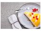 Een stuk cheesecake met mangotopping en rode bessen op een bord met een vork.
