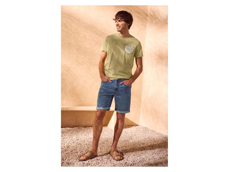 Man in een groen 'summer wave' T-shirt en denim shorts.