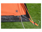 Een oranje tent met een elektrische aansluiting en een haring op gras.