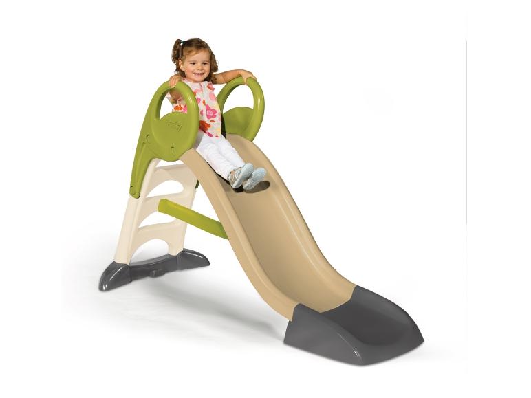 Petite fille souriante glissant sur un toboggan beige et vert.