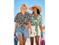 Twee vrouwen in zomerse kleding lopen op het strand met handdoeken.