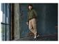 Homme en sweat à capuche vert olive et pantalon cargo beige, appuyé contre un mur.
