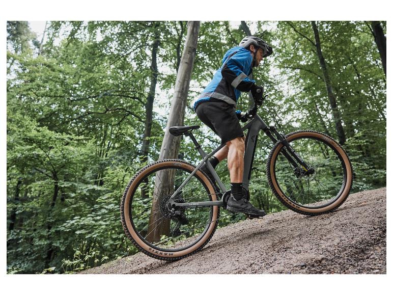 Un homme fait du vélo sur un VTT électrique gris avec des pneus Maxxis dans une forêt.