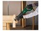 Man met handschoenen zaagt een houten plank met een elektrische reciprozaag op een werkbank.
