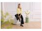 Femme en chemisier jaune à manches longues et pantalon noir, assise sur une chaise blanche.