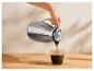 Main versant du café d'un thermos argenté dans un verre sur une table en bois.
