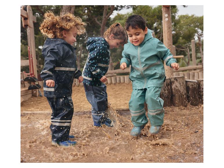 Kinderen spelen in modderplassen met kleurrijke regenjassen.