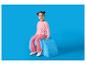Fille en pull et pantalon rose assise sur un pouf bleu.