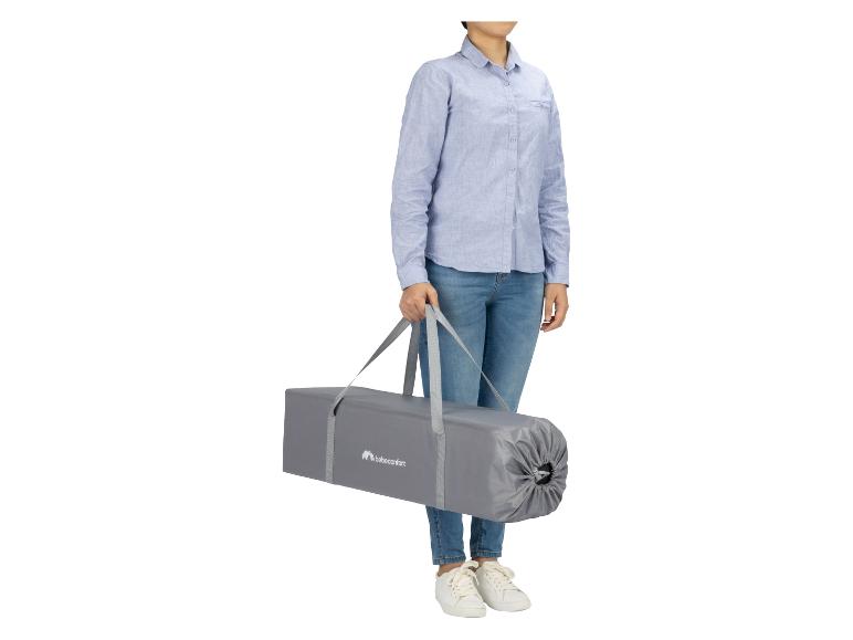 Vrouw draagt een grijze bebeconfort draagtas voor een reiswieg.