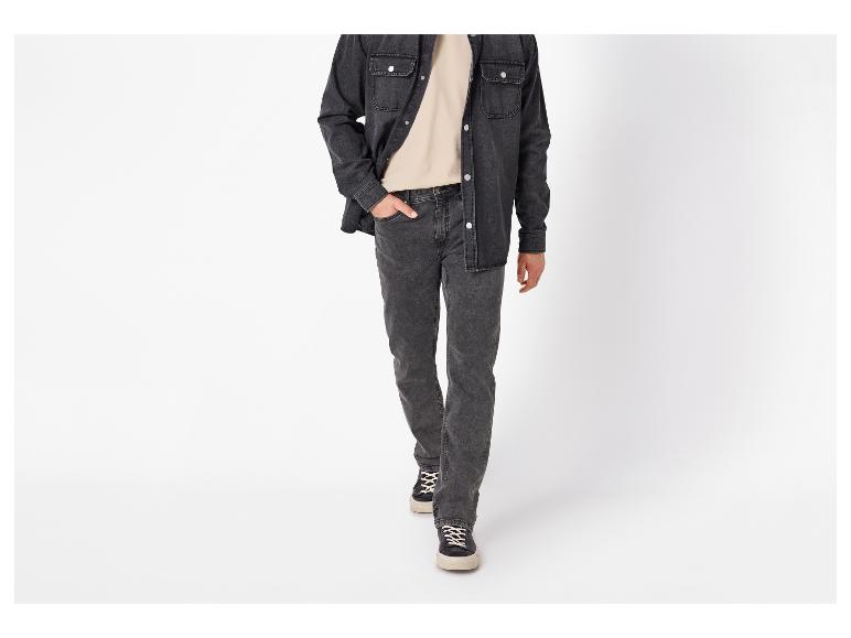 Homme en chemise en jean noire, t-shirt beige et jean gris foncé marchant en avant.