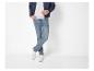 Man in blauwe bomberjack, grijs T-shirt, jeans en witte sneakers.