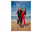 Deux femmes riant en combinaisons à manches courtes, une bleu marine et une rouge, sur la plage.