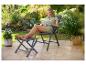 Femme lisant dans une chaise pliante avec repose-pieds sur une terrasse dans le jardin.