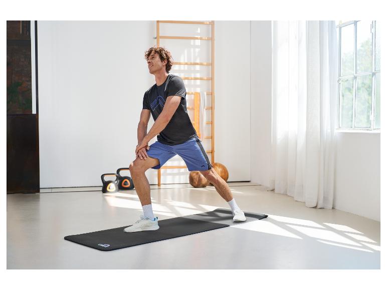 Homme faisant des étirements sur un tapis de sport, portant un t-shirt et un short de sport.