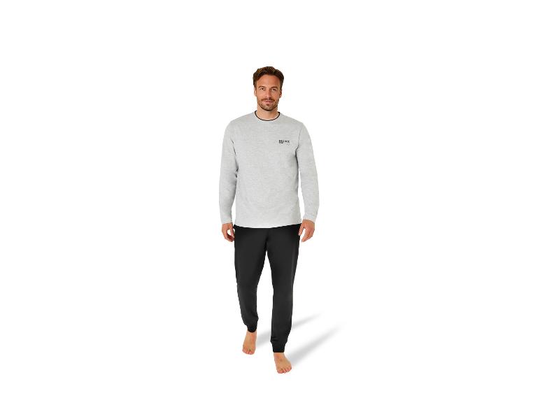 Een man in een lichtgrijs shirt met lange mouwen met 'MEXX 1986'-logo en zwarte joggingbroek.