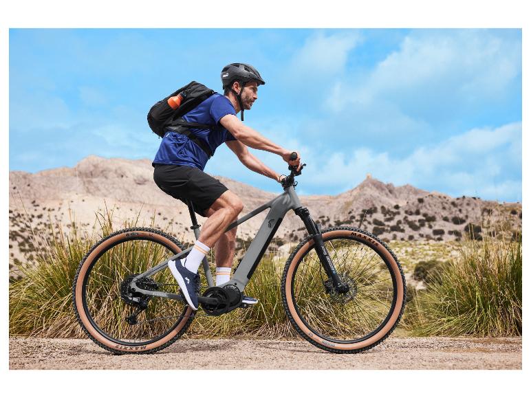 Cycliste sur un VTT électrique avec sac à dos et casque dans un paysage montagneux.