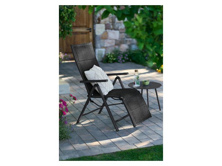 Zwarte tuinstoel met kussen en salontafel op een terras.